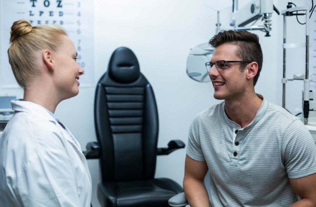 A smiling female optometrist talking to a male patient in an eye exam room.