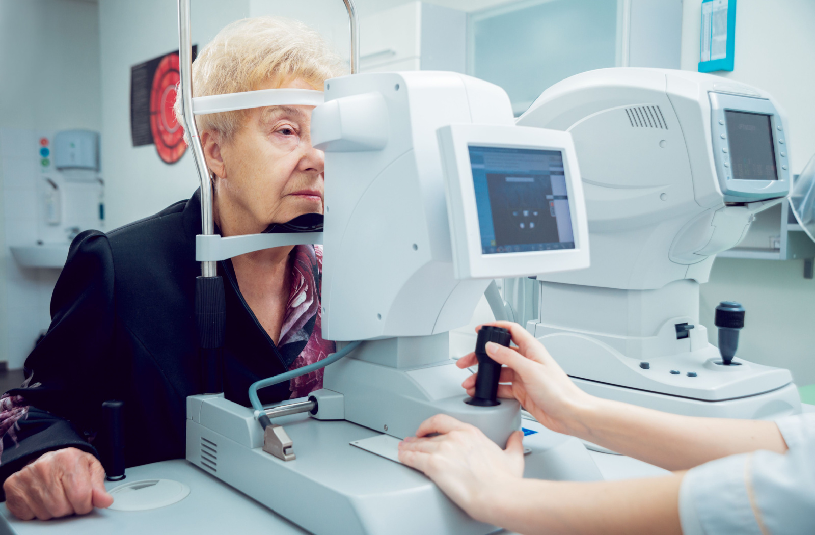 A senior woman sitting in an optometrist's office looking into a machine that tests her vision