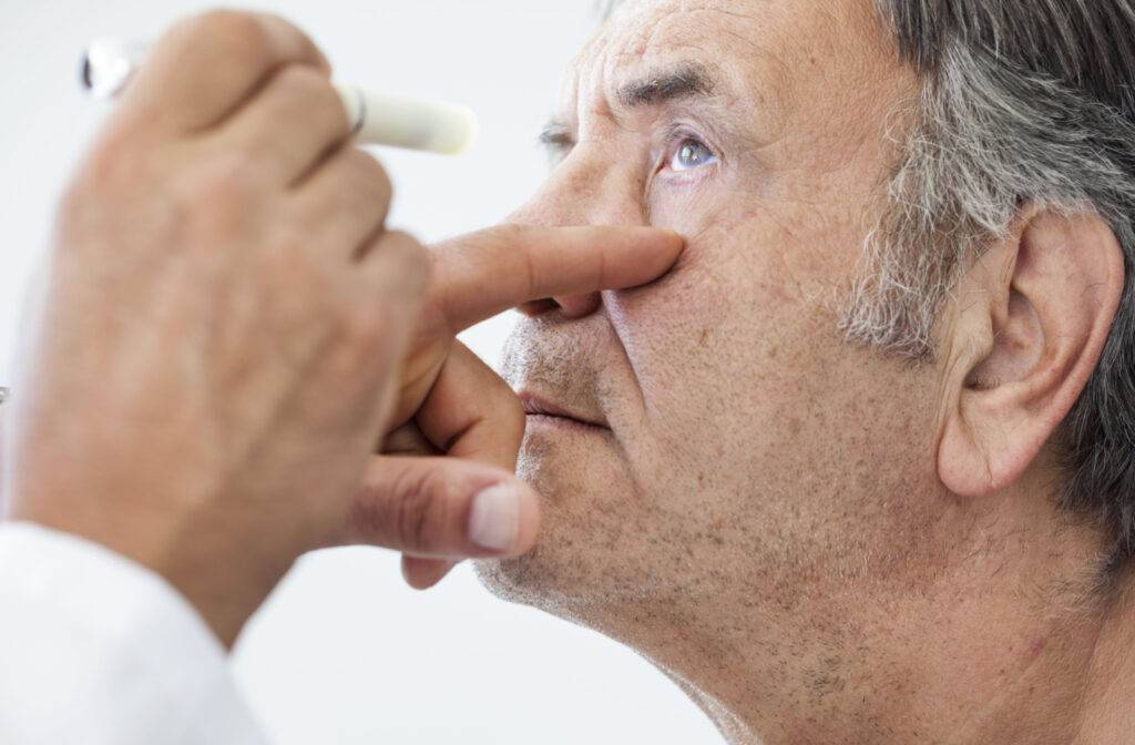 A senior man getting his eyes checked by a doctor who is holding a flash light.